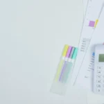 Meja kerja minimalis dengan kalkulator dan dokumen perencanaan anggaran biaya beserta pena warna-warni